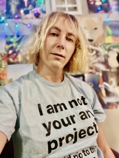 A photo of Lyra McMahon with a blue t-shirt that reads "I am not your art project"